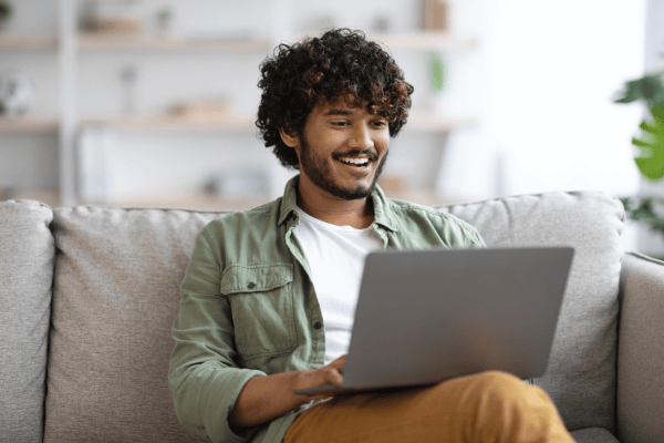 A young man smiling as he uses his laptop