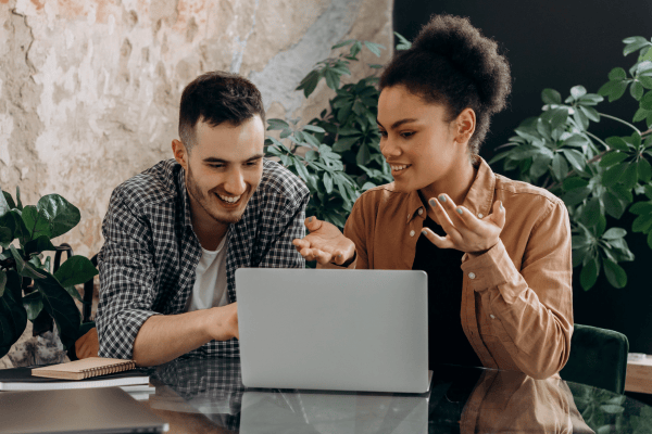 Two coworkers talking and looking at their laptop
